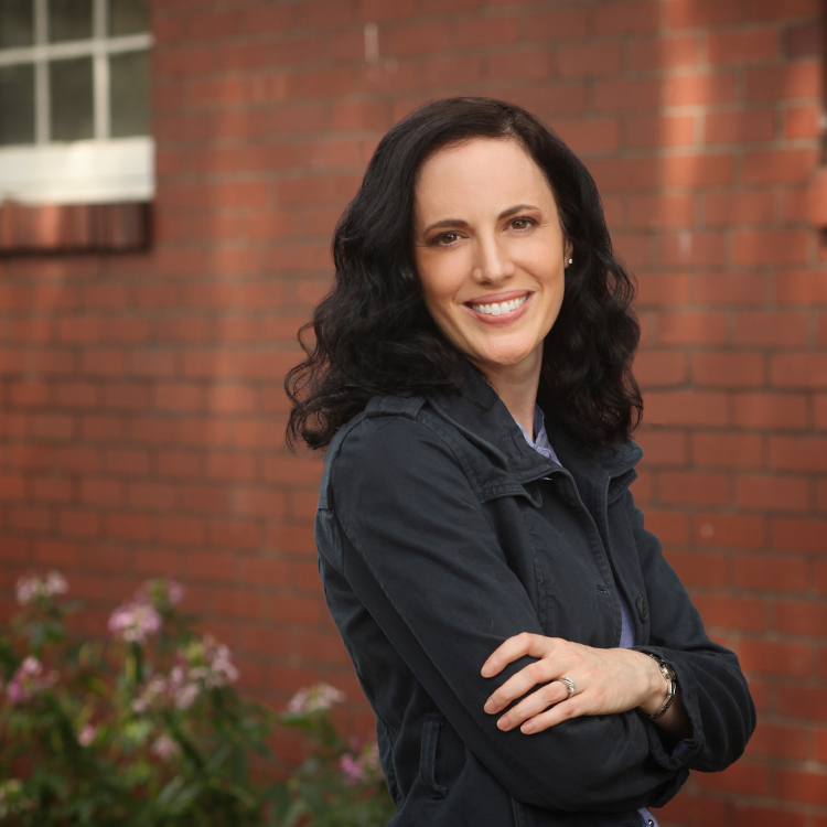 Kathi Finch standing near a brick wall wearing a dark blue jacket